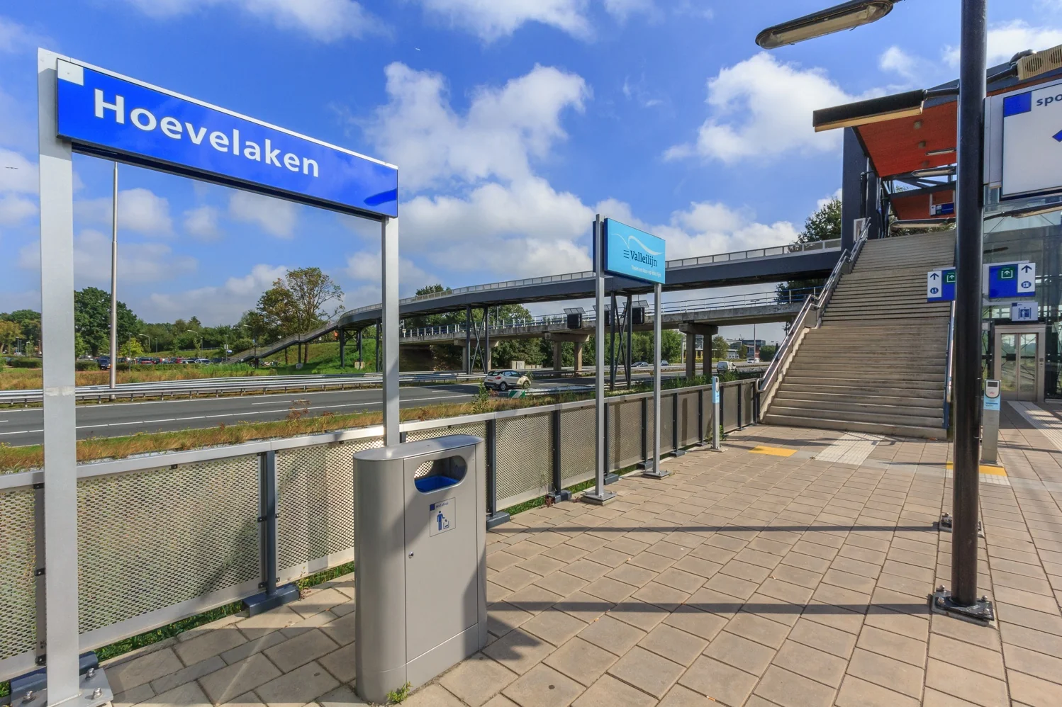 Treinstation Hoevelaken met trapopgang, perronbord en overdekte voetgangersbrug over de snelweg.
